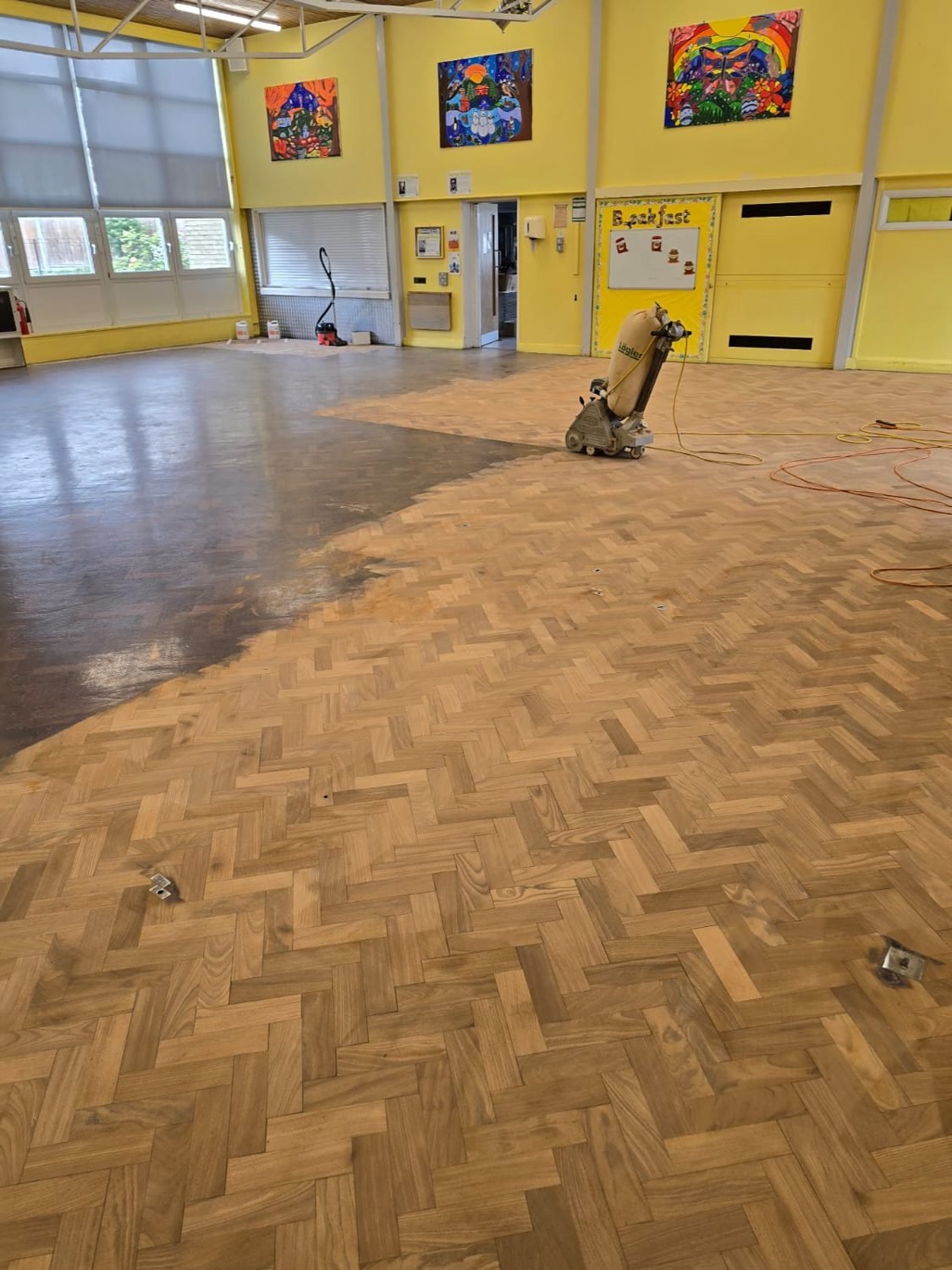 Sanding the parquet floor during restoration at a Croydon school